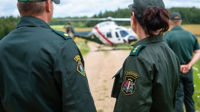Valsts robežsardzes amatpersonas un aiz tām helikopters